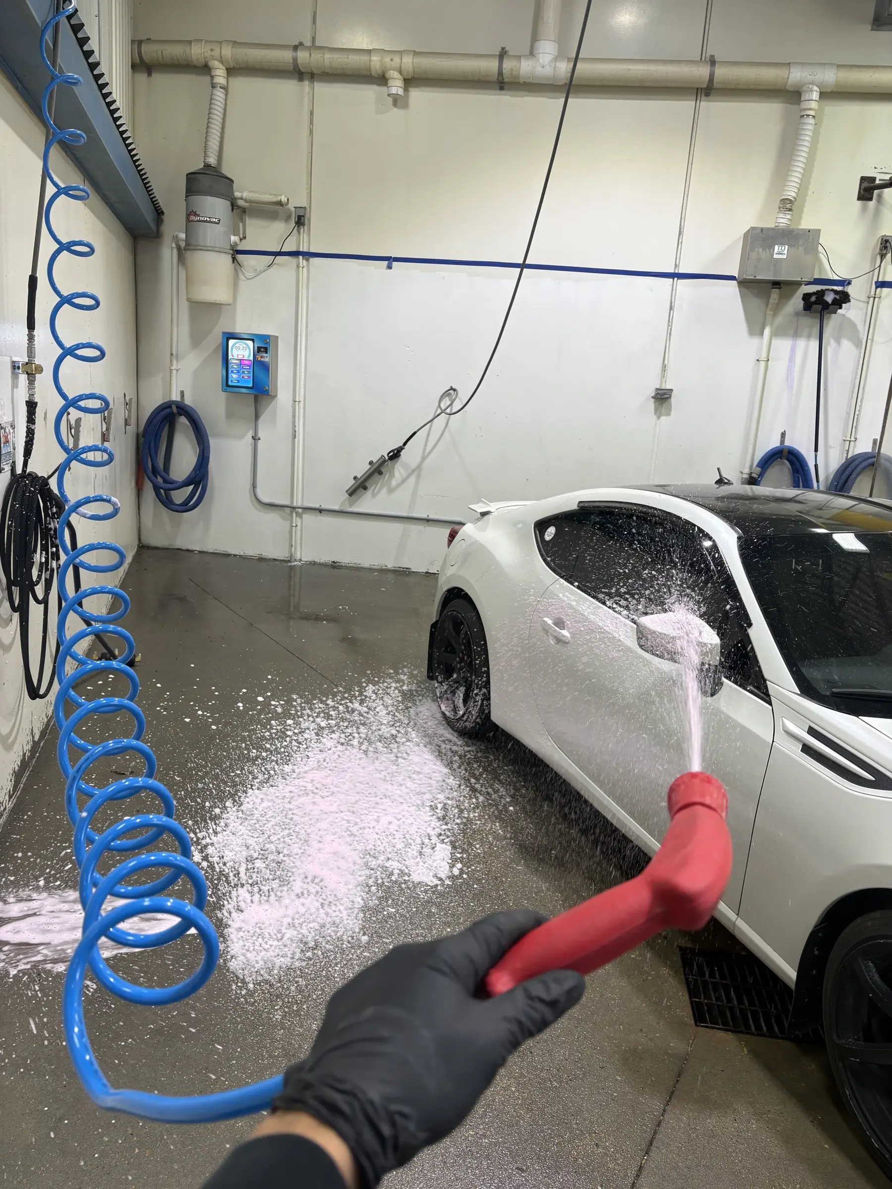 A gloved hand rinsing foam from a white car in a Top Gear self-serve bay