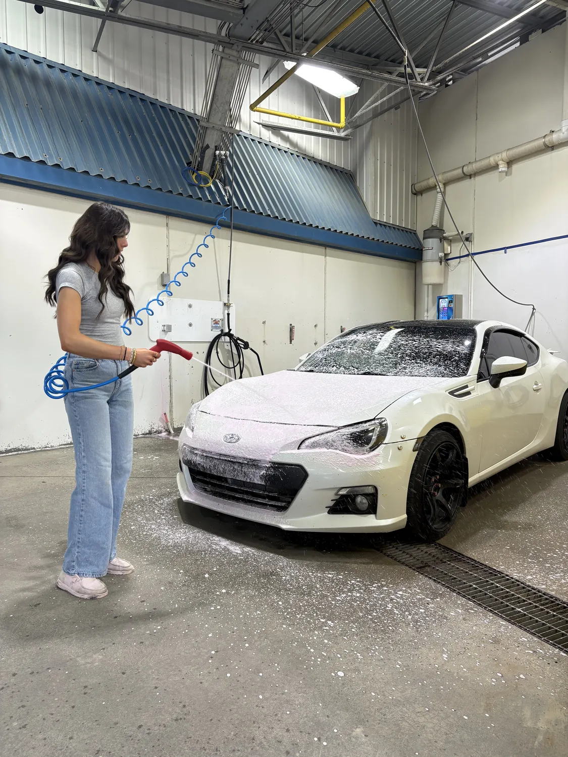 A customer foaming a white car with the wand in a Top Gear self-serve bay